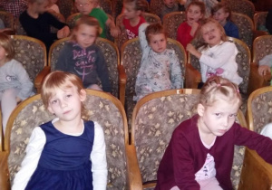 Dzieci siedzące na widowni z zaciekawieniem oglądają przedstawienie.