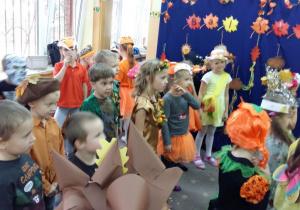 Grupa przedszkolaków w strojach jesiennych tańczą na balu jesieni.