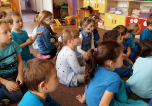 Dzieci ubrane w stroje w kolorze niebieskim, siedzą na dywanie przed tablicą interaktywną. Odpowiadają na pytania nauczyciela na temat praw dziecka.Oglądanie prezentacji o prawach dziecka.