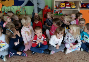 Przedszkolaki oczekują na rozpoczęcie spotkania baletowego. W tle widać zabawki przedszkolne.