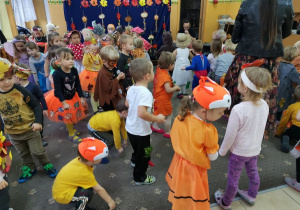 Grupa zadowolonych przedszkolaków tańczy na balu jesieni w przygotowanych na tą okazję strojach.