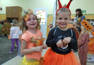 Dwie uśmiechnięte dziewczynki - jedna w stroju wiewiórki, druga w stroju Pani Jesieni, pozują do zdjęcia.