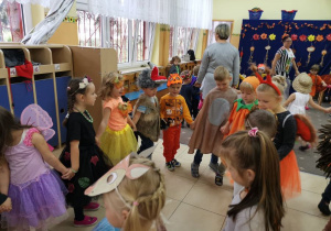 Grupa zadowolonych przedszkolaków w strojach przygotowanych na bal jesienie tańczy w kole.