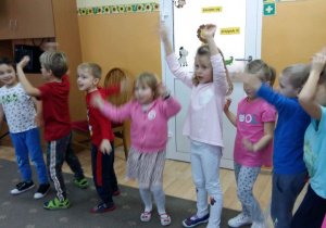 Dzieci ustawione w półkolu, podnoszą ręce w górę podczas zabawy mikołajkowej.