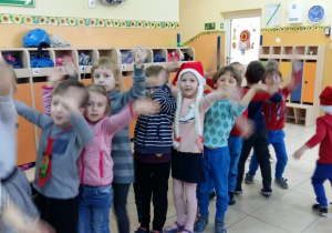 Dzieci stojące jedno za drugim , podnoszą ręce w górę podczas zabawy mikołajkowej.