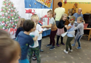 Dzieci bawią się podczas zabawy mikołajkowej w parach. W tle widoczna jest dekoracja świąteczna.
