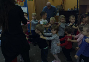 Dzieci bawią się podczas zabawy mikołajkowej. Dzieci poruszają się po sali ustawione jedno za drugim w tzw. „pociąg”. Prowdząca bal wspólnie z przedszkolakiem "tworzą most" pod którym przechodzą dzieci.