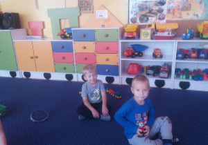 Chłopcy bawią się na dywanie.W tle widoczne są meble przedszkolne i zabawki