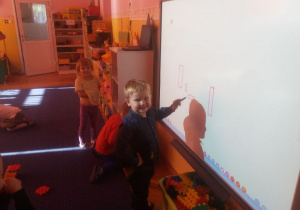 Chłopiec rysuje na tablicy interaktywnej. Obok bawią sie inne dzieci.