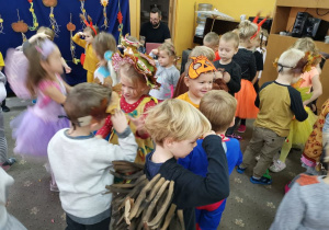 Dzieci tańczą w szatni przedszkolnej na balu jesieni. Dzieci poprzebierane są w stroje lisków, wiewiórek, grzybków. W tle widoczne są szafki z ubraniami dzieci.