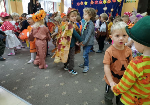 Dzieci tańczą w parach w szatni przedszkolnej na balu jesieni. Dzieci poprzebierane są w stroje "jesienne" itd. W tle widoczne są szafki z ubraniami dzieci.