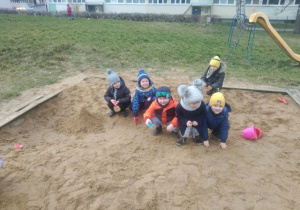 Dzieci z grupy drugiej w piaskownicy w ogrodzie przedszkolnym. Dzieci trzymają w rękach akcesoria do zabaw w piasku.