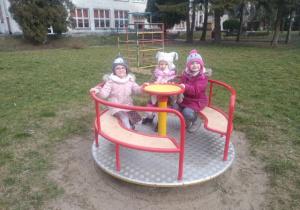 Dzieci z grupy drugiej siedzą na karuzeli w ogrodzie przedszkolnym.