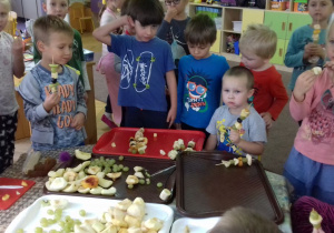 Dzieci jedzą przygotowane przez siebie szaszłyki owocowe.