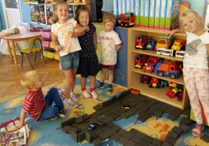 Dzieci układają wzory z czarnych kwadratów piankowych.