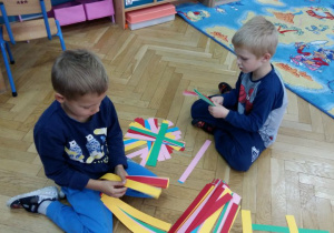 Dzieci układają na dywanie wzory z pasków z papieru.