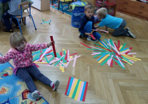 Dzieci układają na dywanie wzory z pasków z papieru.