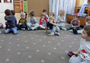 Dzieci siedzą na dywanie podczas zabawy mikołajkowej