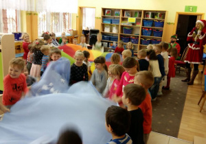 Dzieci w kole trzymając niebieski materiał, podrzucają do góry kulki z papieru
