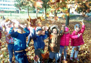 Roześmiane przedszkolaki podczas jesiennych zabaw w ogrodzie przedszkolnym podrzucają do góry kolorowe liście.