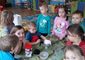 Dzieci siedzą przy stole w sali przedszkolnej, sprawdzają czystość śniegu.