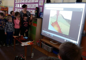 Dzieci oglądają prezentację na temat wulkanów na tablicy multimedialnej.