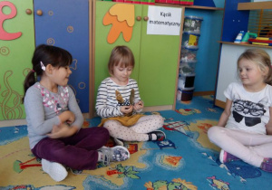 Dzieci siedzą na dywanie w sali przedszkolnej i oglądają meteoryt.