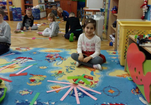 Dzieci układają na dywanie wzory (kwiat) z kolorowych pasków papieru.