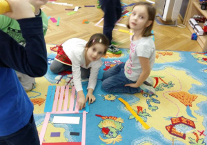Dzieci układają na dywanie wzory z kolorowych pasków papieru.