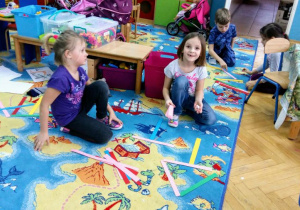 Dzieci układają na dywanie wzory z kolorowych pasków papieru.