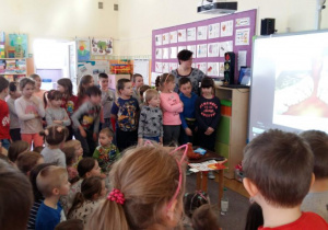 Dzieci oglądają prezentację na temat wulkanu. W tle widoczne są tablice dydaktyczne, meble przedszkolne i zabawki.