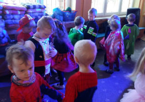 Dzieci przebrane w stroje karnawałowe bawią się na balu. W tle widać szafki w szatni przedszkolnej.