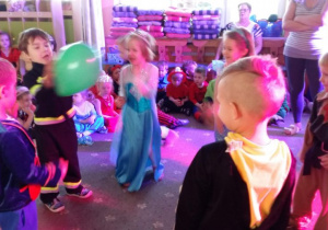 Dzieci ubrane w stroje karnawałowe, podają balon podczas konkursu.