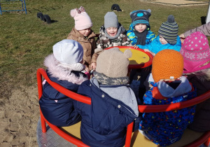 Dzieci siedzą na karuzeli w ogrodzie przedszkolnym.
