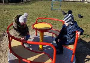 2 dzieci siedzą na karuzeli w ogrodzie przedszkolnym.