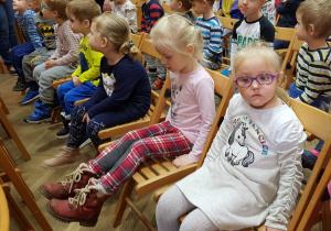 Dzieci siedzą w sali teatralnej domu kultury, oczekując na rozpoczęcie przedstawienia.