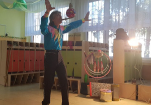 Akrobata stoi w szatni przedszkolnej i prezentuje pokaz ekwilibrystyki: balans na nożu.