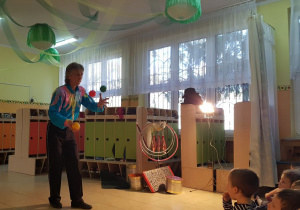 Akrobata w szatni przedszkolnej prezentuje pokaz ekwilibrystyki: żonglerkę piłeczkami.