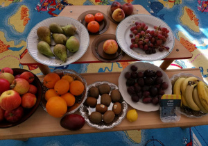 Prezentacja owoców: jabłka, banany, brzoskwinie, pomarańcze, borówki, gruszki, śliwki, winogrona czerwone.