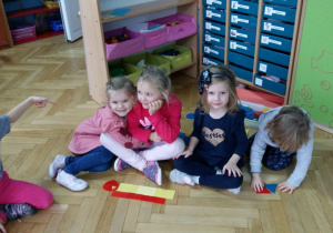 Dzieci siedzą na dywanie i układają figury geometryczne