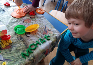 Chłopiec przy stole lepi z ciastoliny. Na stole rozłożone są foremki do zabaw plastycznych.