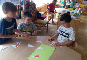 Dzieci siedzą przy stoliku i układają puzzle- godło Polski.