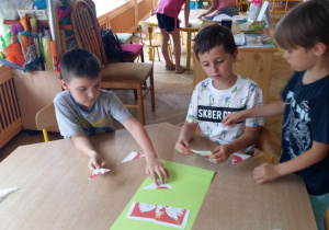 Dzieci siedzą przy stoliku i układają puzzle- godło Polski.