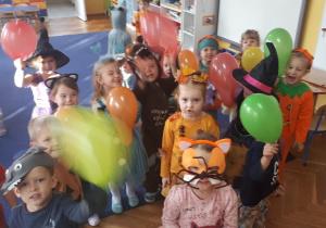 Dzieci przebrane na bal jesieni pozują do zdjęcia z balonami.