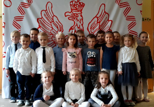 Dzieci z grupy IV na tle biało - czerwonej dekoracji.