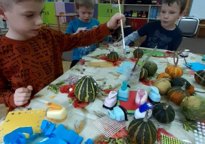 Dzieci siedzą przy stoliku i przyklejaja ozdoby na dynie