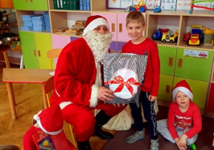 Chłopiec w czerwonej bluzce pozuje z Mikołajem i prezentem