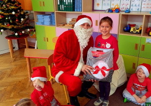 Dziewczynka w czerwonej bluzce pozuje z Mikołajem i prezentem