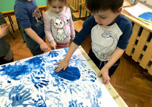 Dzieci odciskają dłoń, umoczoną w niebieskiej farbie na kartce papieru