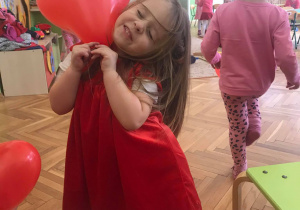 Dziewczynka ubrana w czerwoną sukienkę, trzyma w rękach balon